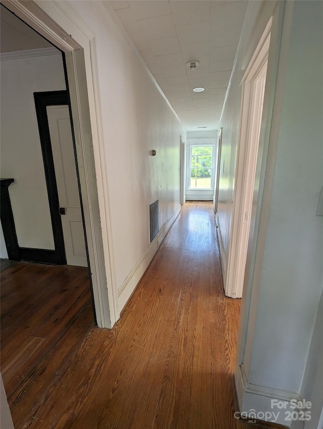 corridor with visible vents, wood finished floors, baseboards, and ornamental molding