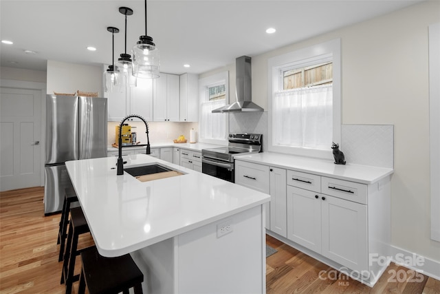 kitchen with light wood-style flooring, a sink, appliances with stainless steel finishes, a kitchen breakfast bar, and wall chimney exhaust hood