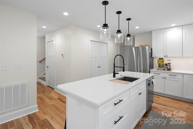 kitchen featuring visible vents, light wood-style flooring, a sink, stainless steel appliances, and light countertops