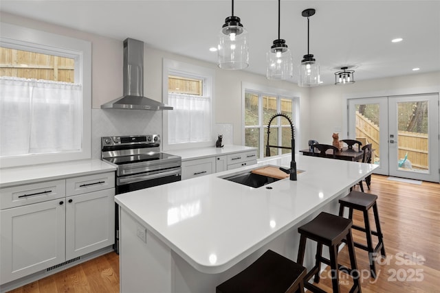 kitchen featuring visible vents, wall chimney range hood, light wood-style floors, electric range, and a sink