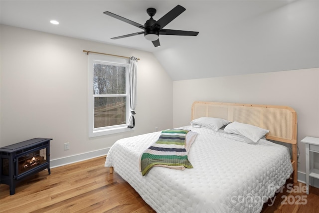 bedroom featuring baseboards, vaulted ceiling, recessed lighting, a wood stove, and wood finished floors