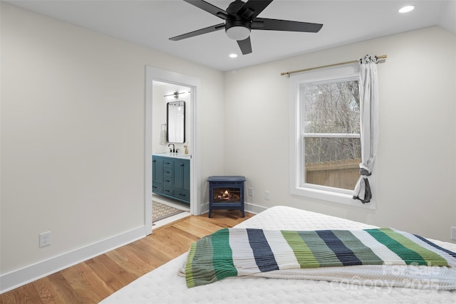 bedroom featuring light wood-type flooring, a wood stove, baseboards, and a sink