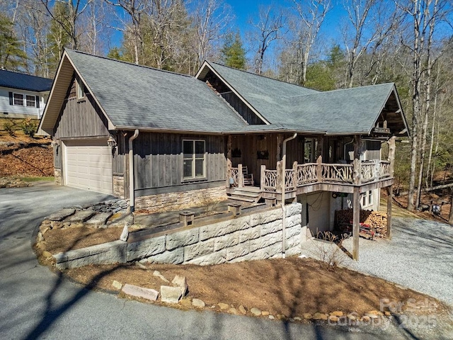 chalet / cabin with aphalt driveway, stone siding, board and batten siding, roof with shingles, and a garage