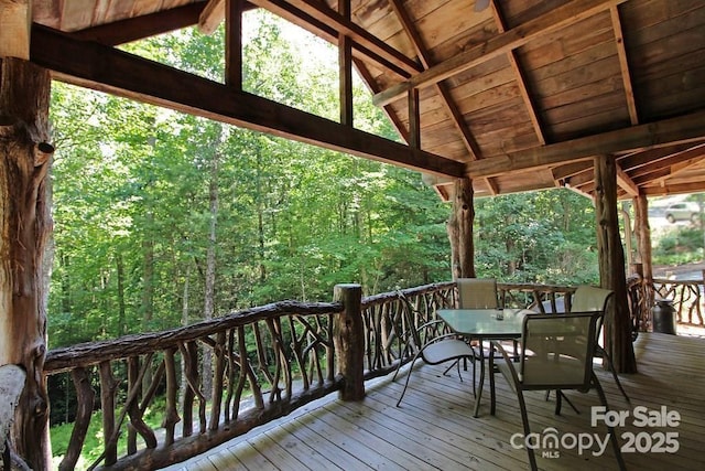 deck with outdoor dining area and a wooded view