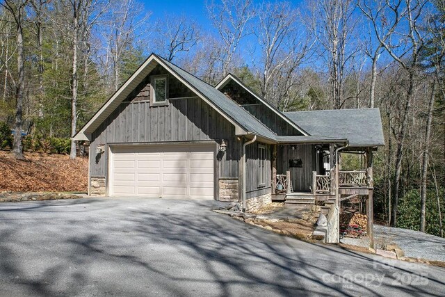 rustic home with driveway, roof with shingles, a porch, an attached garage, and stone siding