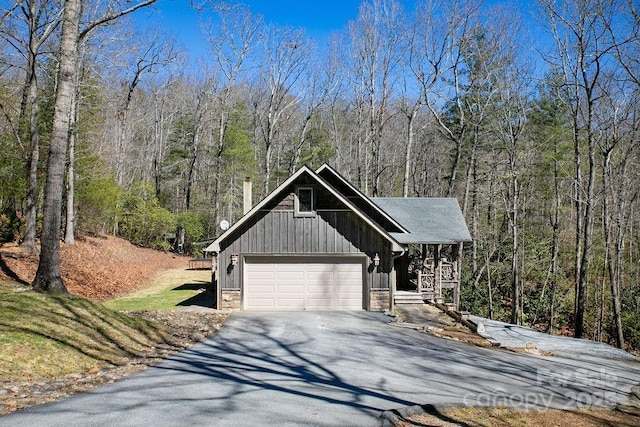 view of front of property with driveway, an attached garage, stone siding, a view of trees, and board and batten siding