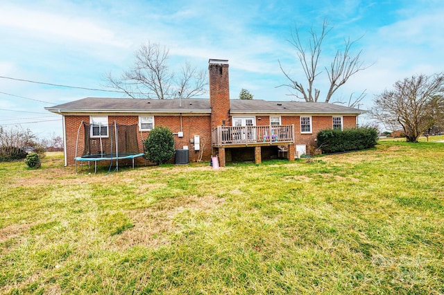 rear view of house with brick siding, a trampoline, a chimney, a yard, and a deck