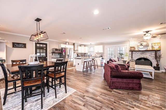 dining space featuring wood finished floors, visible vents, a fireplace, ornamental molding, and french doors