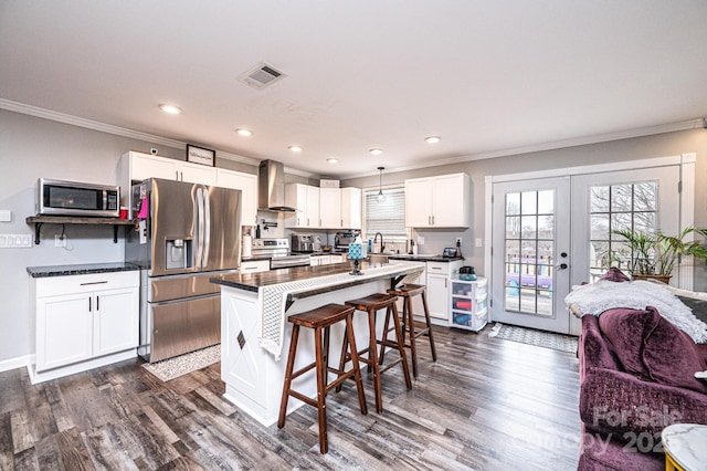 kitchen featuring dark countertops, stainless steel appliances, french doors, a breakfast bar area, and wall chimney range hood