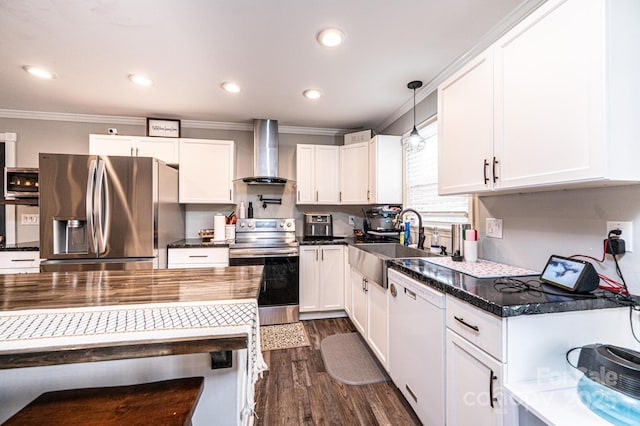 kitchen with a sink, ornamental molding, stainless steel appliances, white cabinets, and wall chimney range hood