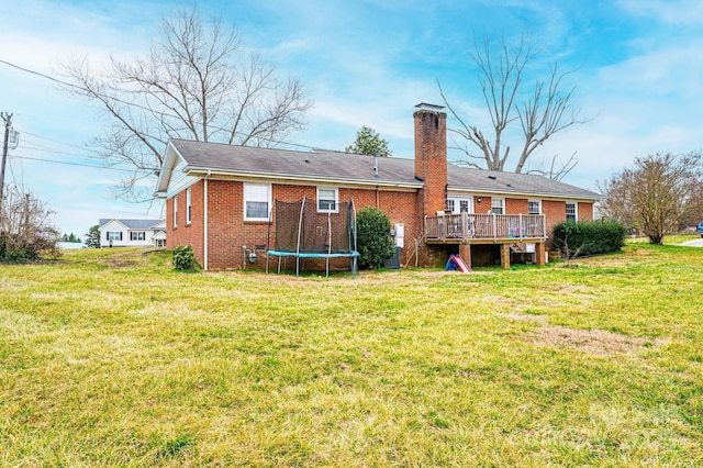 rear view of house featuring a lawn, a deck, a trampoline, brick siding, and a chimney