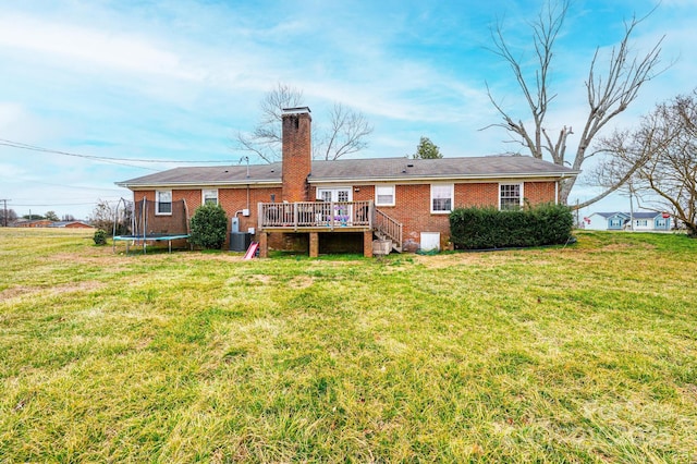 rear view of house featuring a deck, a trampoline, a lawn, and brick siding