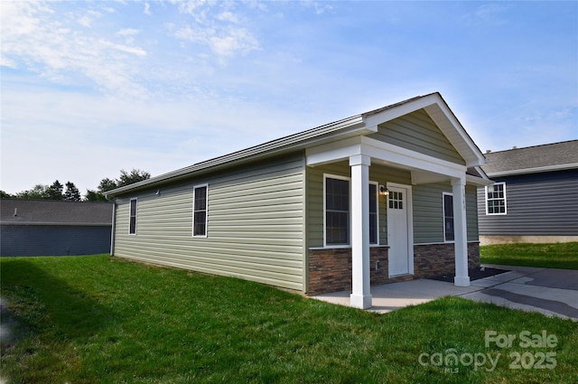 view of side of home featuring stone siding, a patio, and a yard