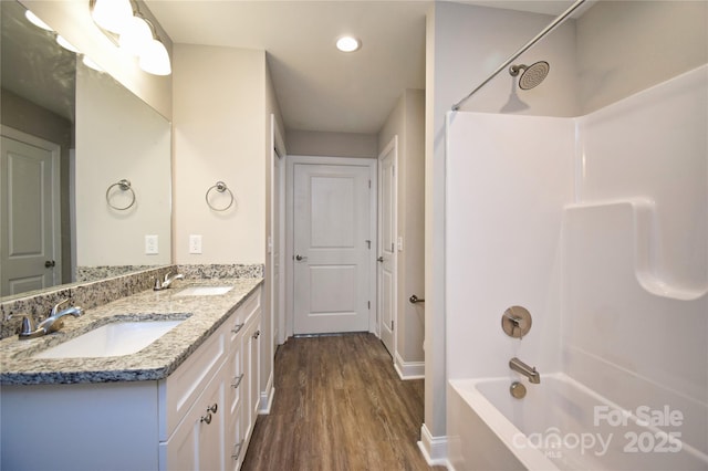 bathroom with a sink, double vanity, wood finished floors, and bathtub / shower combination