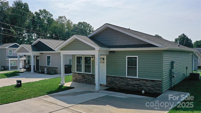 craftsman house with a front yard, cooling unit, stone siding, and roof with shingles