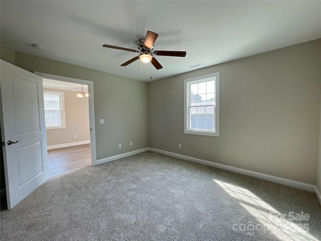 carpeted spare room with visible vents, baseboards, and ceiling fan