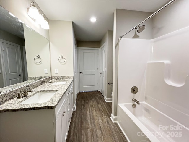 full bath featuring double vanity, wood finished floors, bathing tub / shower combination, and a sink