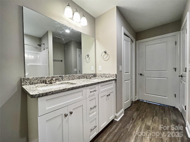 bathroom featuring a sink, a shower, wood finished floors, and double vanity