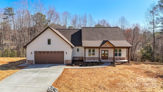 modern farmhouse featuring a garage, stone siding, roof with shingles, and driveway