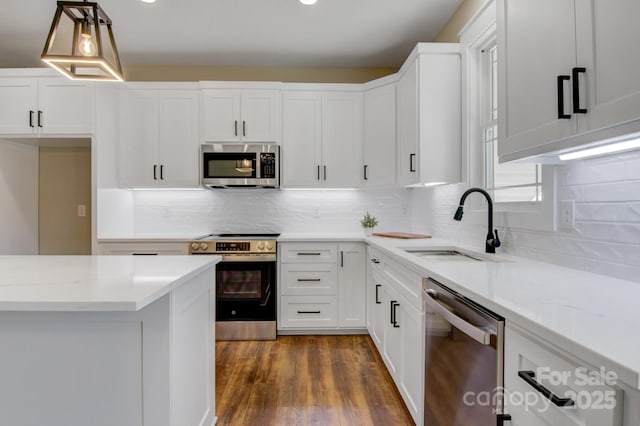 kitchen featuring decorative light fixtures, decorative backsplash, stainless steel appliances, white cabinetry, and a sink