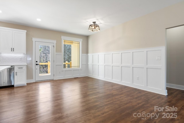 unfurnished dining area with a wainscoted wall, dark wood-type flooring, and a decorative wall