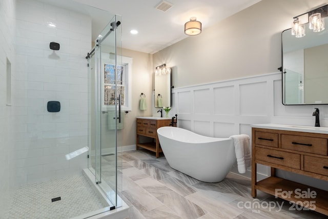 full bathroom with visible vents, a shower stall, a freestanding tub, a decorative wall, and vanity