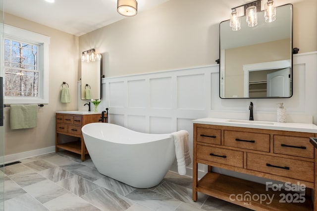 full bath with visible vents, a decorative wall, two vanities, a soaking tub, and a sink