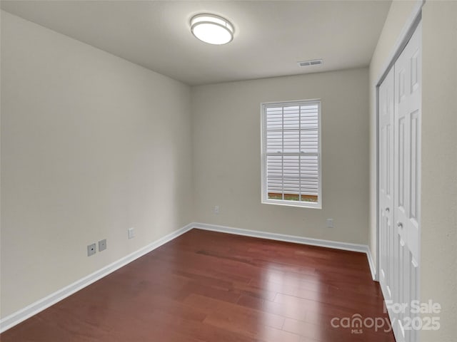 unfurnished bedroom featuring dark wood finished floors, visible vents, baseboards, and a closet