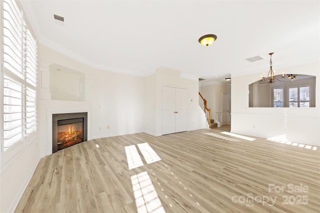 unfurnished living room with visible vents, stairway, ornamental molding, wood finished floors, and a glass covered fireplace