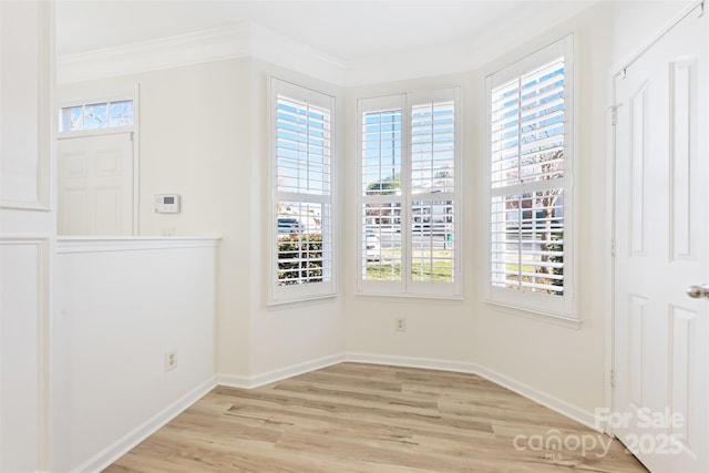 unfurnished dining area with light wood-style flooring, crown molding, and baseboards