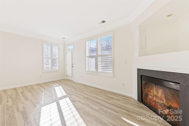 unfurnished living room featuring visible vents, a glass covered fireplace, crown molding, and light wood-style flooring