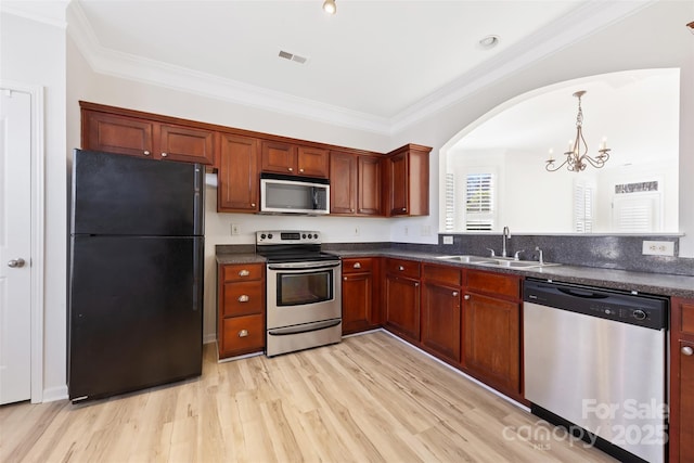 kitchen featuring dark countertops, ornamental molding, light wood-style flooring, appliances with stainless steel finishes, and a sink