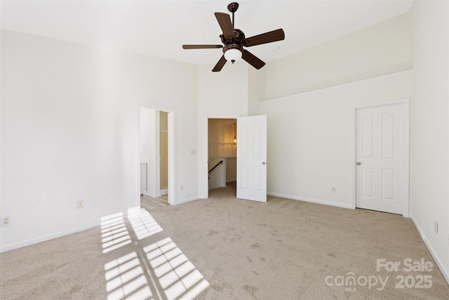 unfurnished bedroom with a walk in closet, baseboards, light colored carpet, ensuite bathroom, and high vaulted ceiling