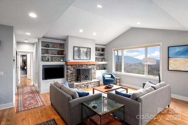 living area with a fireplace, baseboards, light wood-type flooring, and lofted ceiling