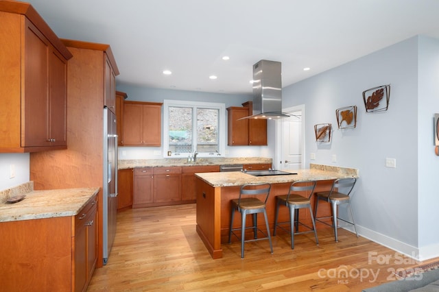 kitchen featuring brown cabinets, a kitchen breakfast bar, island exhaust hood, a peninsula, and black electric cooktop