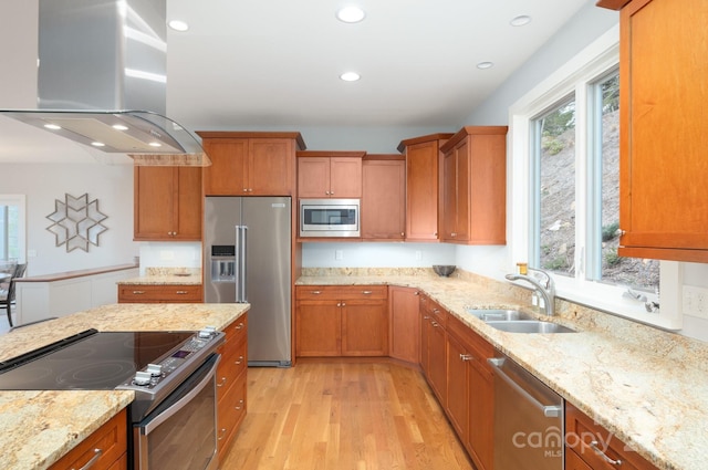 kitchen with light wood finished floors, a sink, stainless steel appliances, brown cabinetry, and island range hood