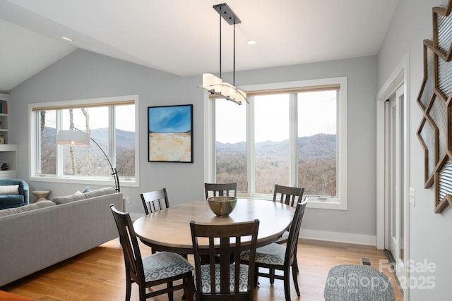 dining space featuring baseboards, a healthy amount of sunlight, light wood-style flooring, and vaulted ceiling