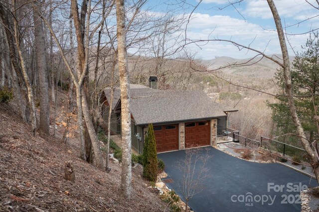 exterior space with aphalt driveway, stone siding, a mountain view, an attached garage, and a shingled roof