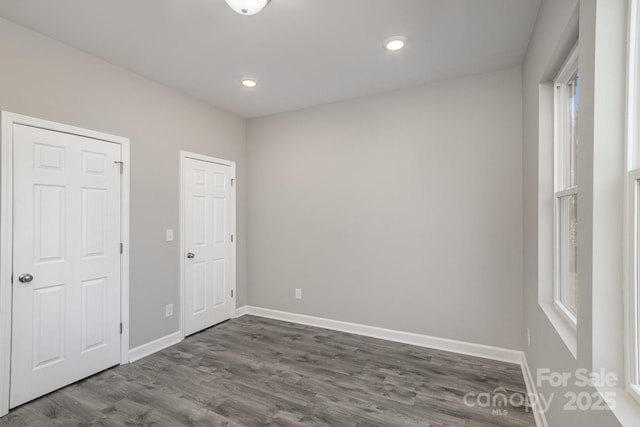 unfurnished bedroom featuring multiple windows, baseboards, and dark wood-style flooring