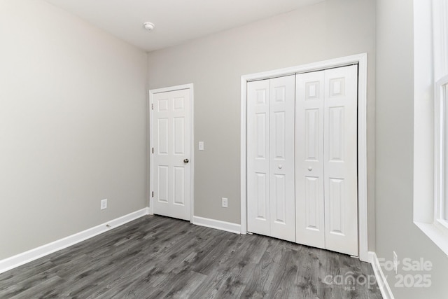 unfurnished bedroom with baseboards, dark wood-style flooring, and a closet