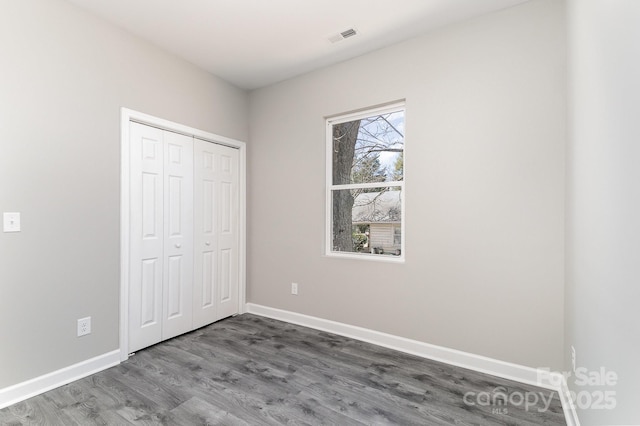 unfurnished bedroom with a closet, visible vents, baseboards, and wood finished floors