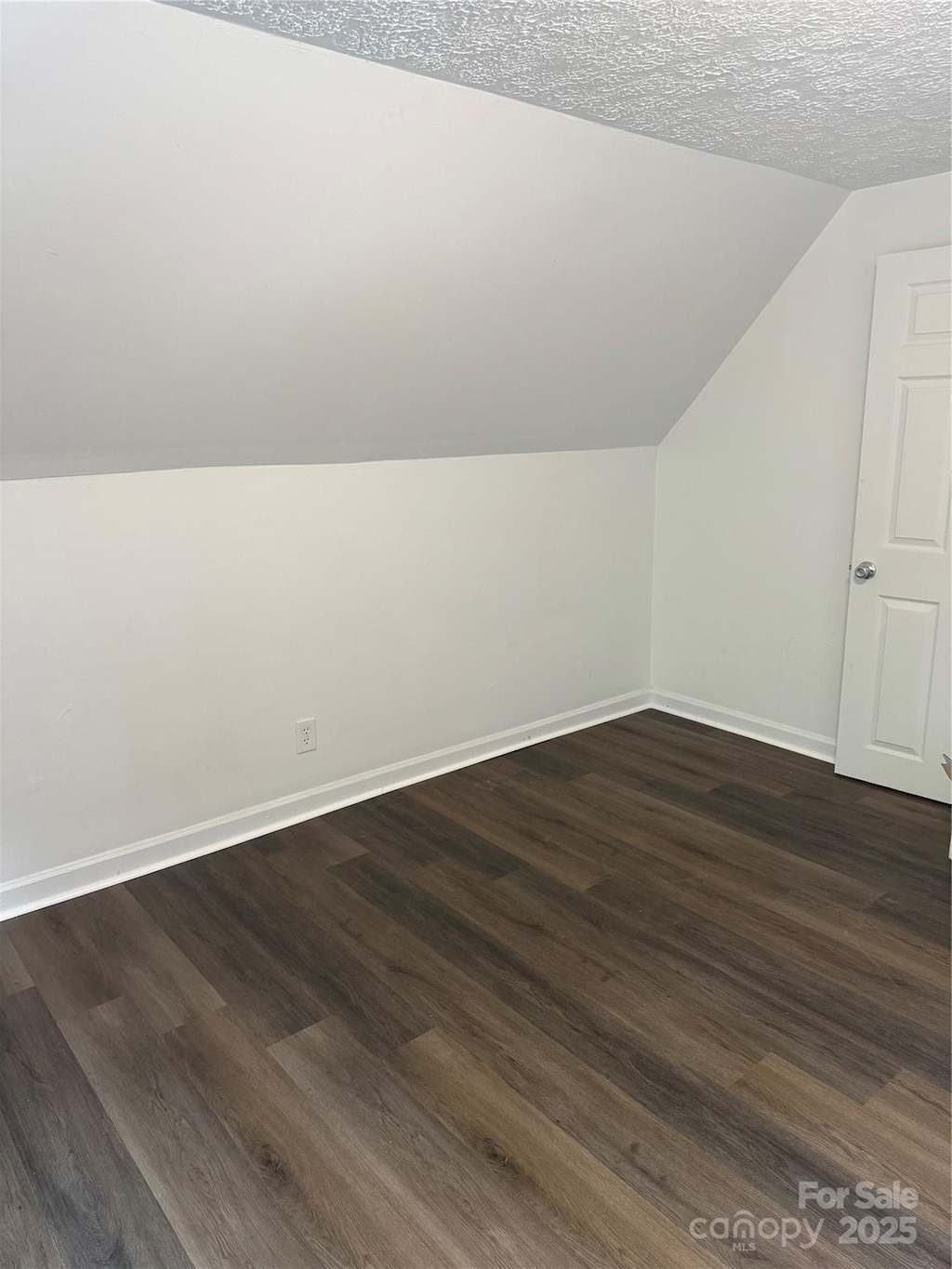 bonus room featuring dark wood finished floors, a textured ceiling, baseboards, and vaulted ceiling