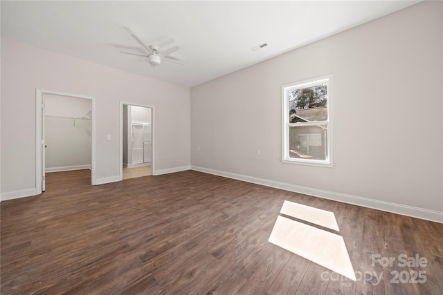 unfurnished bedroom featuring a walk in closet, a closet, baseboards, ceiling fan, and dark wood-style flooring