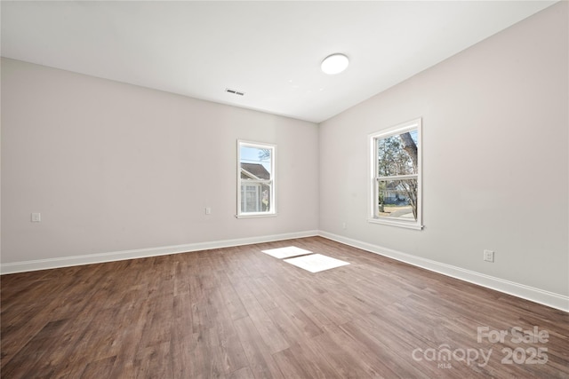 unfurnished room with a wealth of natural light, visible vents, baseboards, and wood finished floors