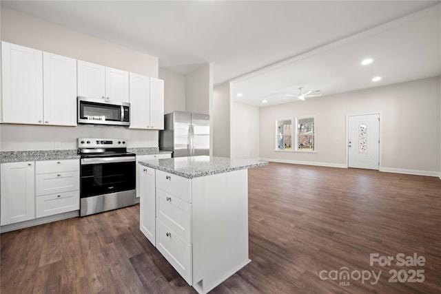 kitchen featuring a center island, light stone counters, appliances with stainless steel finishes, white cabinets, and dark wood-style flooring