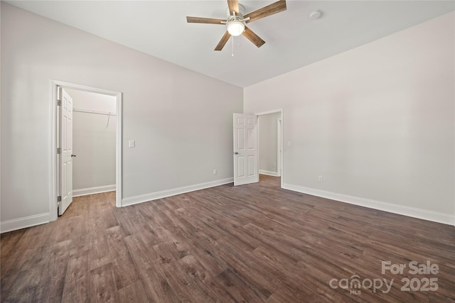 unfurnished bedroom featuring a spacious closet, dark wood-type flooring, baseboards, lofted ceiling, and a ceiling fan