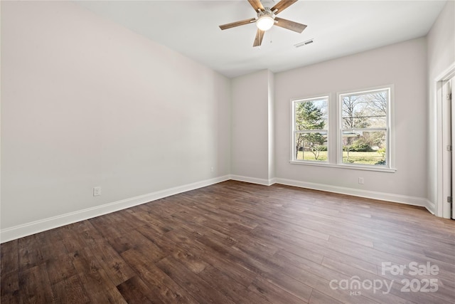 spare room featuring dark wood-type flooring, a ceiling fan, visible vents, and baseboards