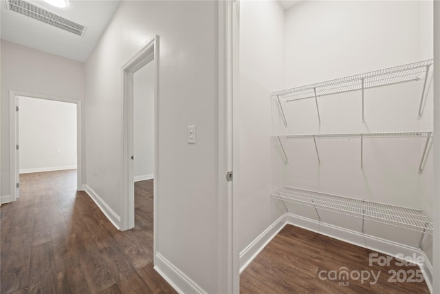 hallway with dark wood-style floors, visible vents, and baseboards