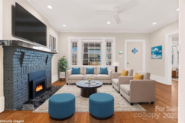 living area featuring a fireplace, crown molding, baseboards, and hardwood / wood-style flooring