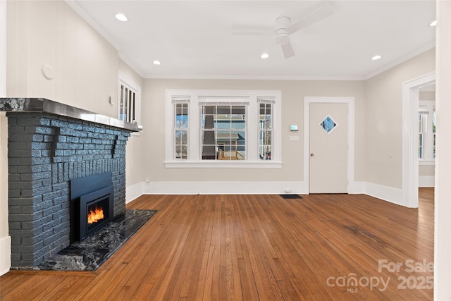 unfurnished living room featuring wood-type flooring, ceiling fan, a fireplace, and crown molding